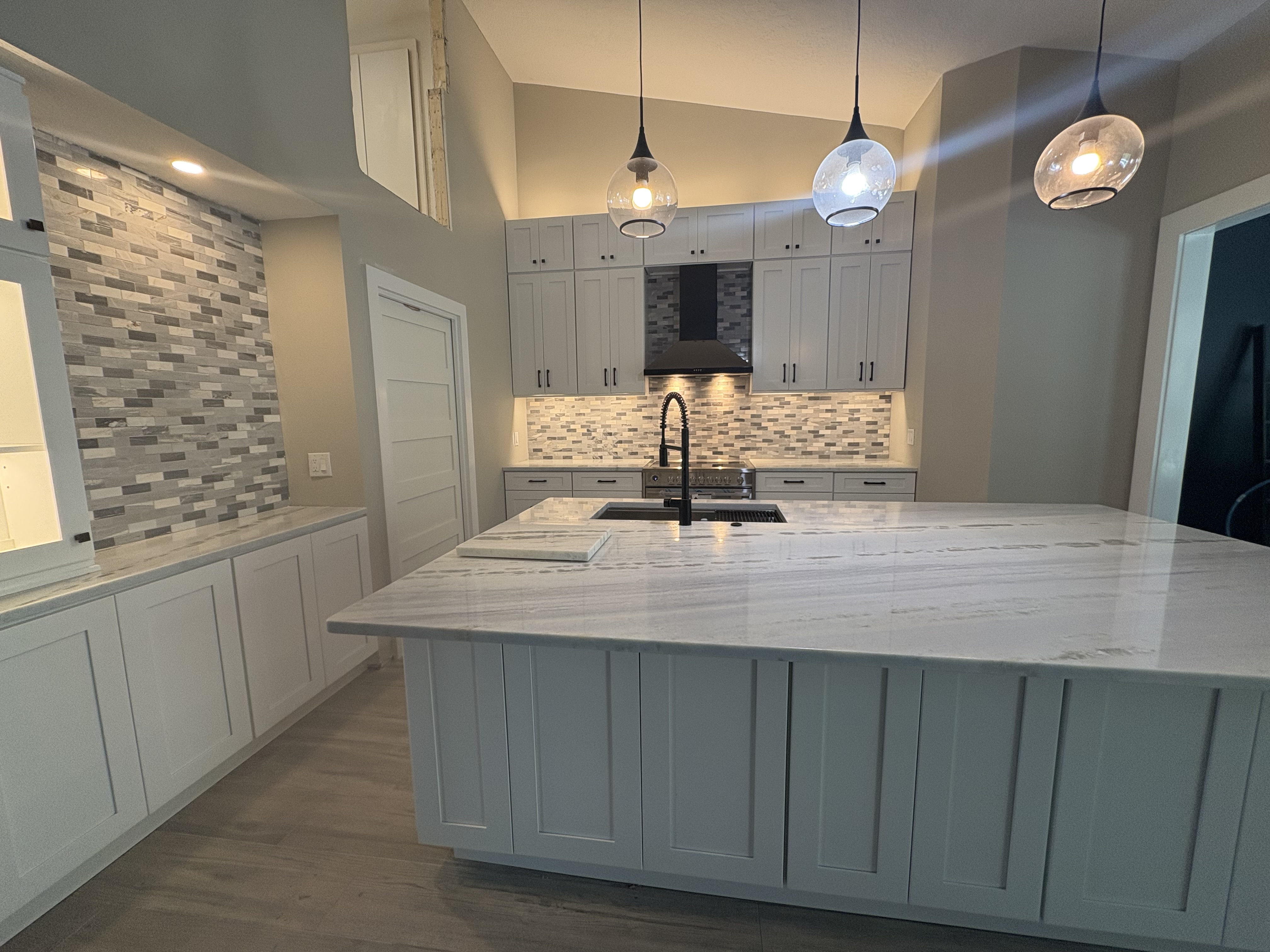 Open-concept kitchen with marble island, glass tile backsplash, and globe pendant lights