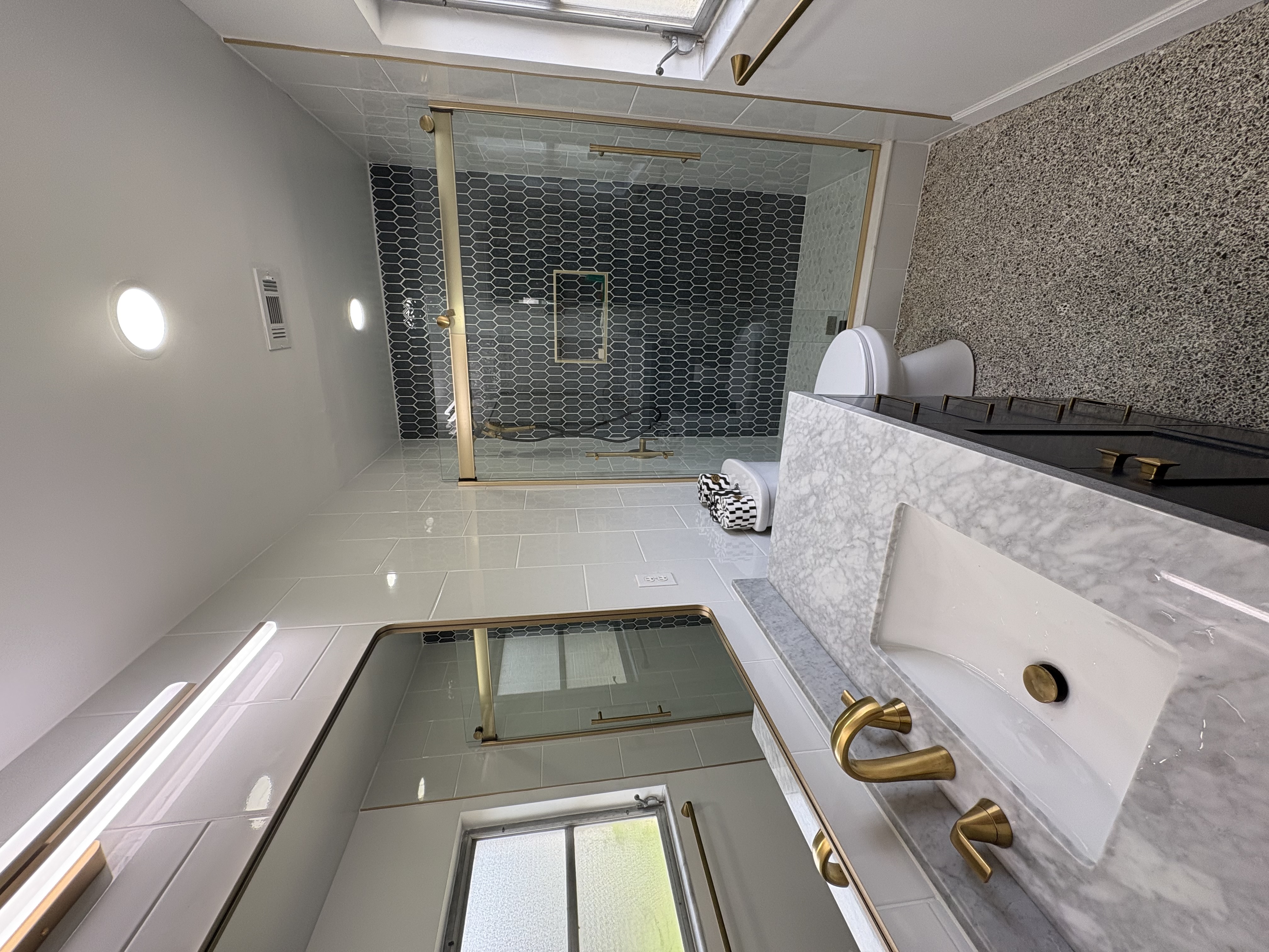 Luxury bathroom with dark hexagonal tile shower, brass-framed glass enclosure, and marble vanity