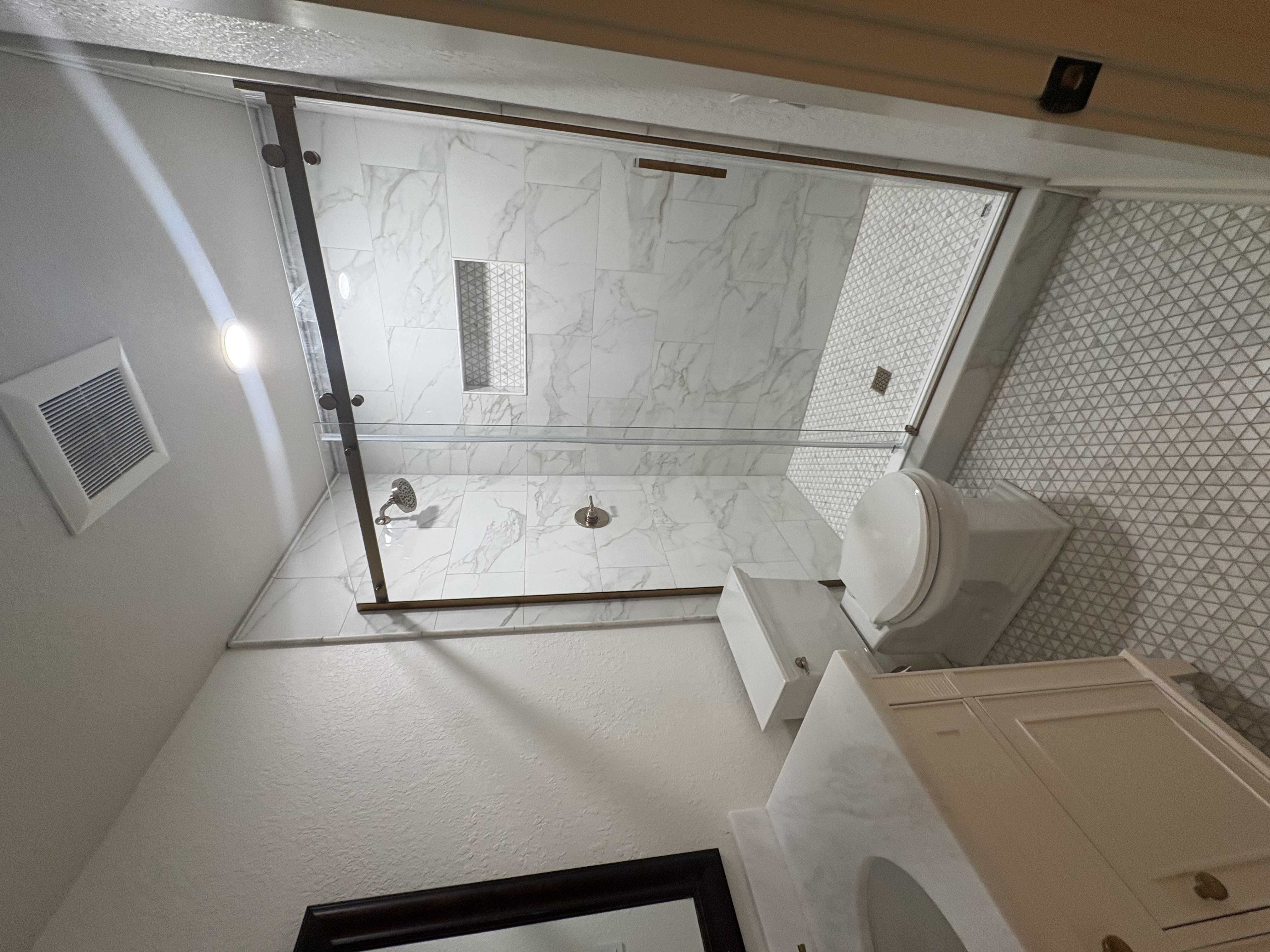 Bathroom with marble-look porcelain tile shower, frameless glass door, and geometric accent wall