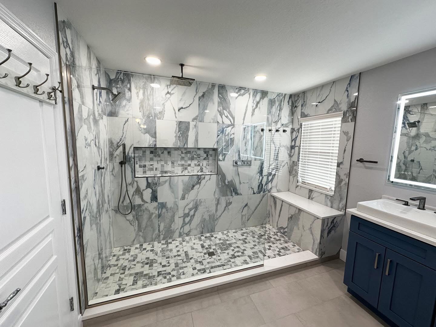 Dramatic marble slab walk-in shower with mosaic floor tile and navy blue vanity