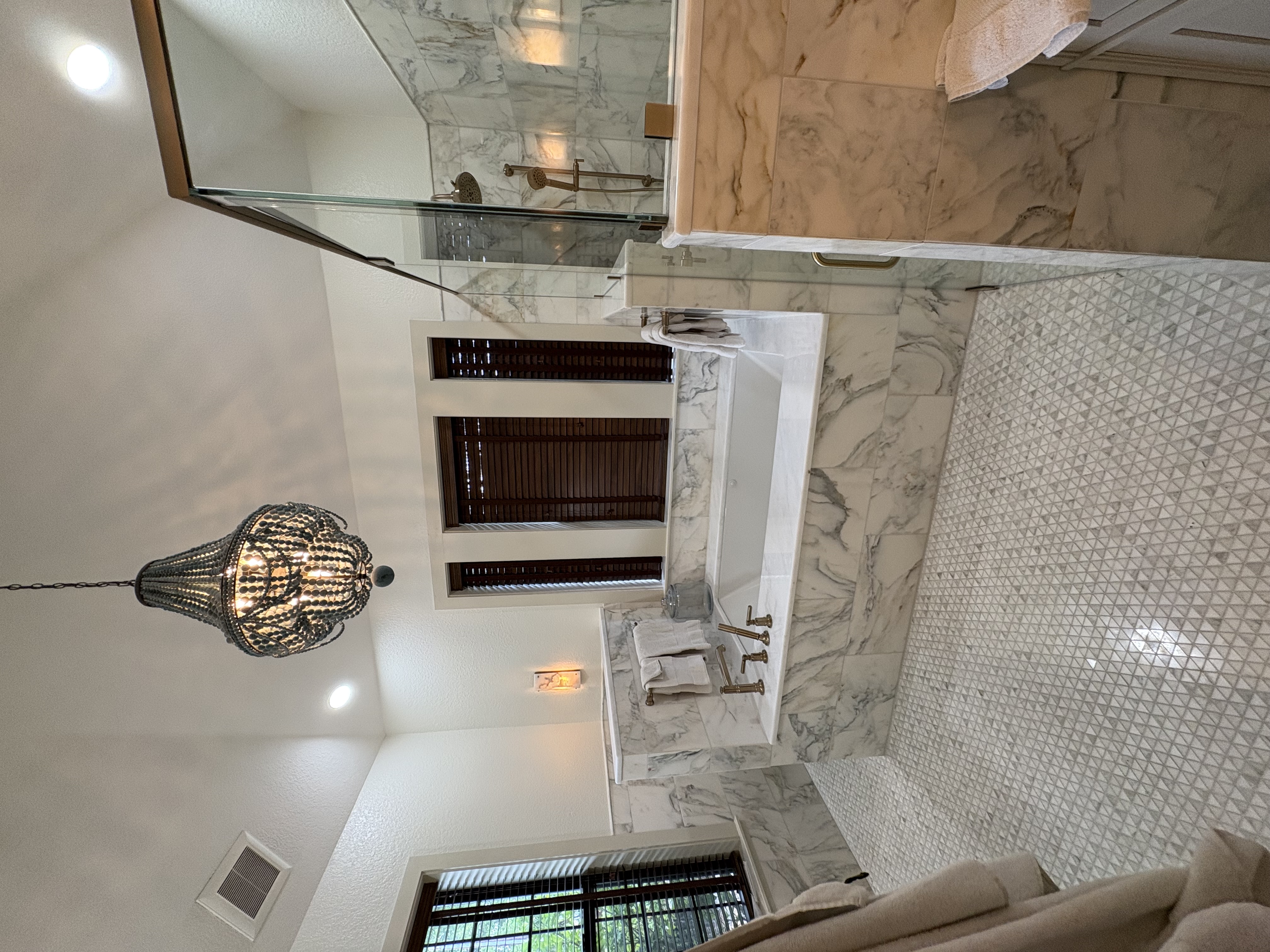 Luxury master bathroom with marble walls, chandelier, freestanding tub, and glass shower