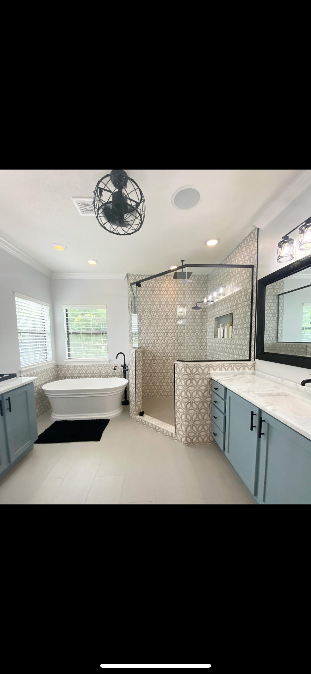 Spacious bathroom with freestanding tub, geometric tile walk-in shower, and blue vanities