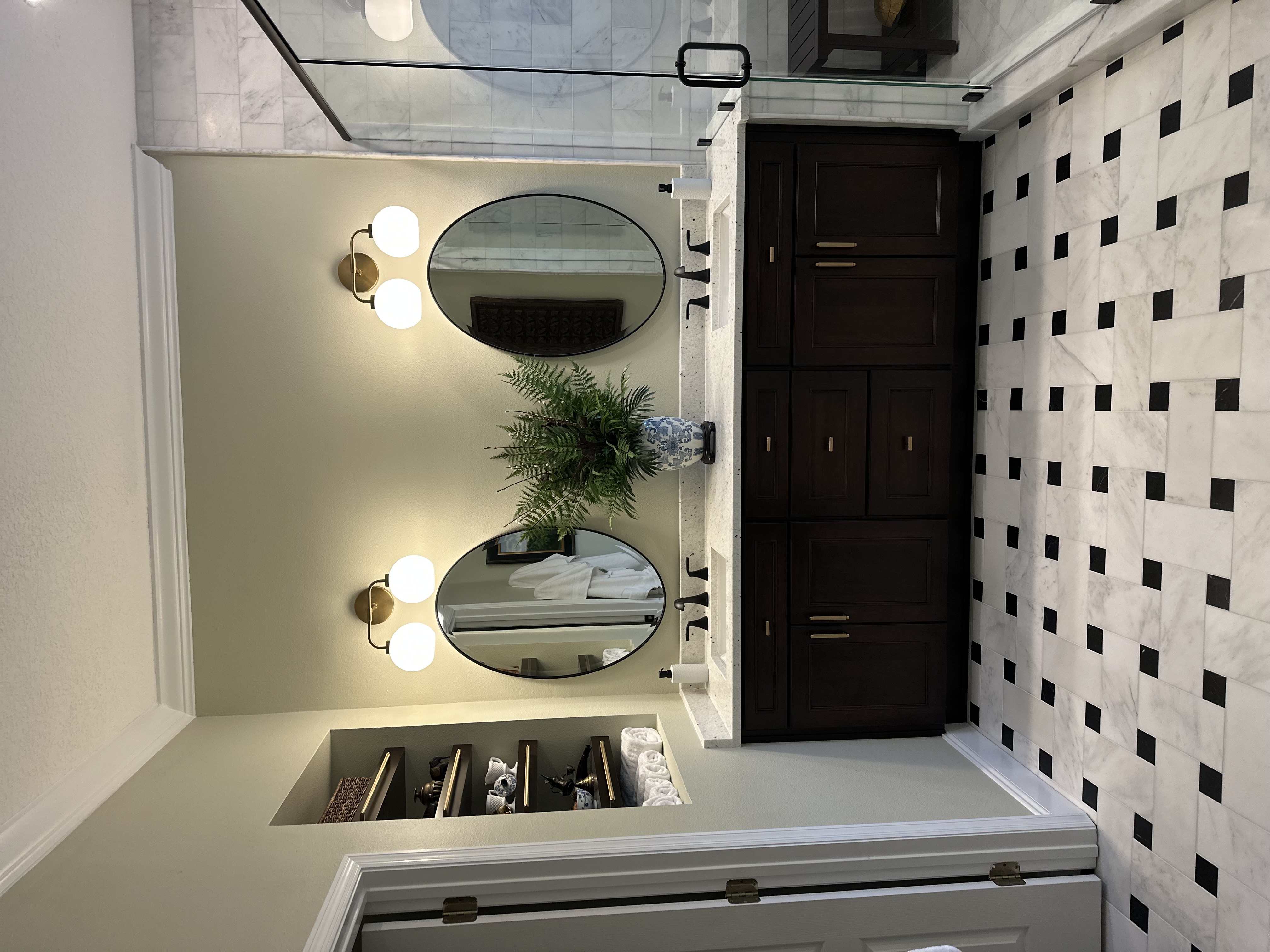 Elegant bathroom with dual oval mirrors, marble tile accent wall, and dark wood storage tower