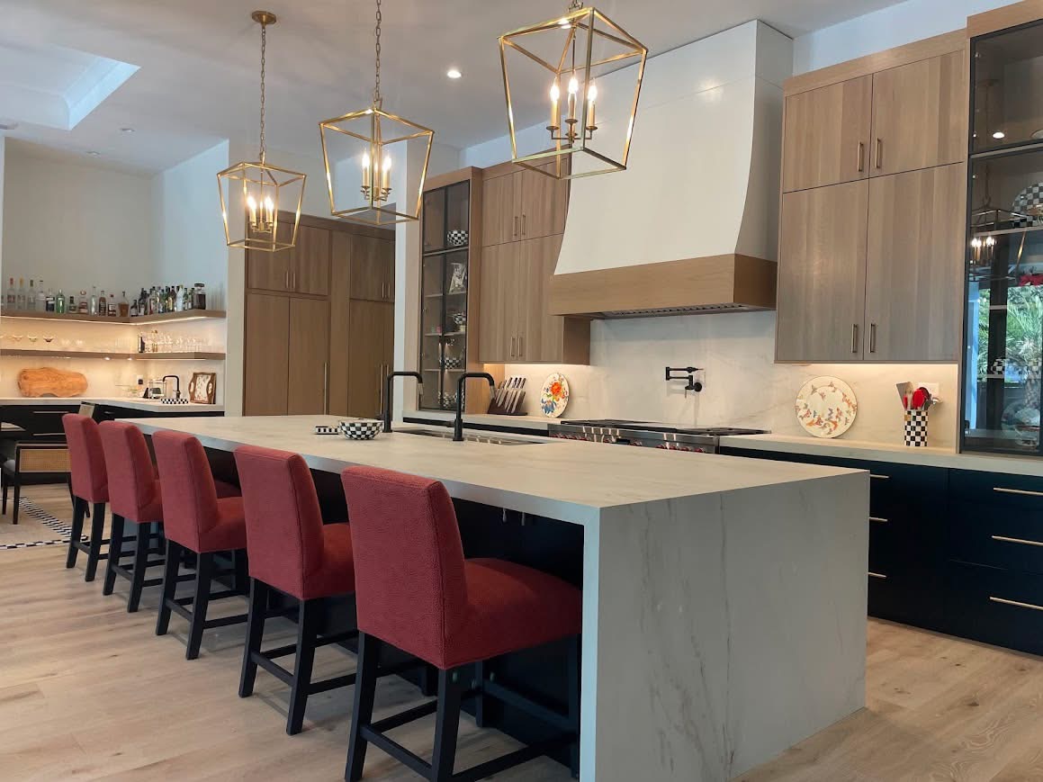 Modern kitchen with red upholstered bar chairs, gold cage pendant lights, and two-tone cabinetry