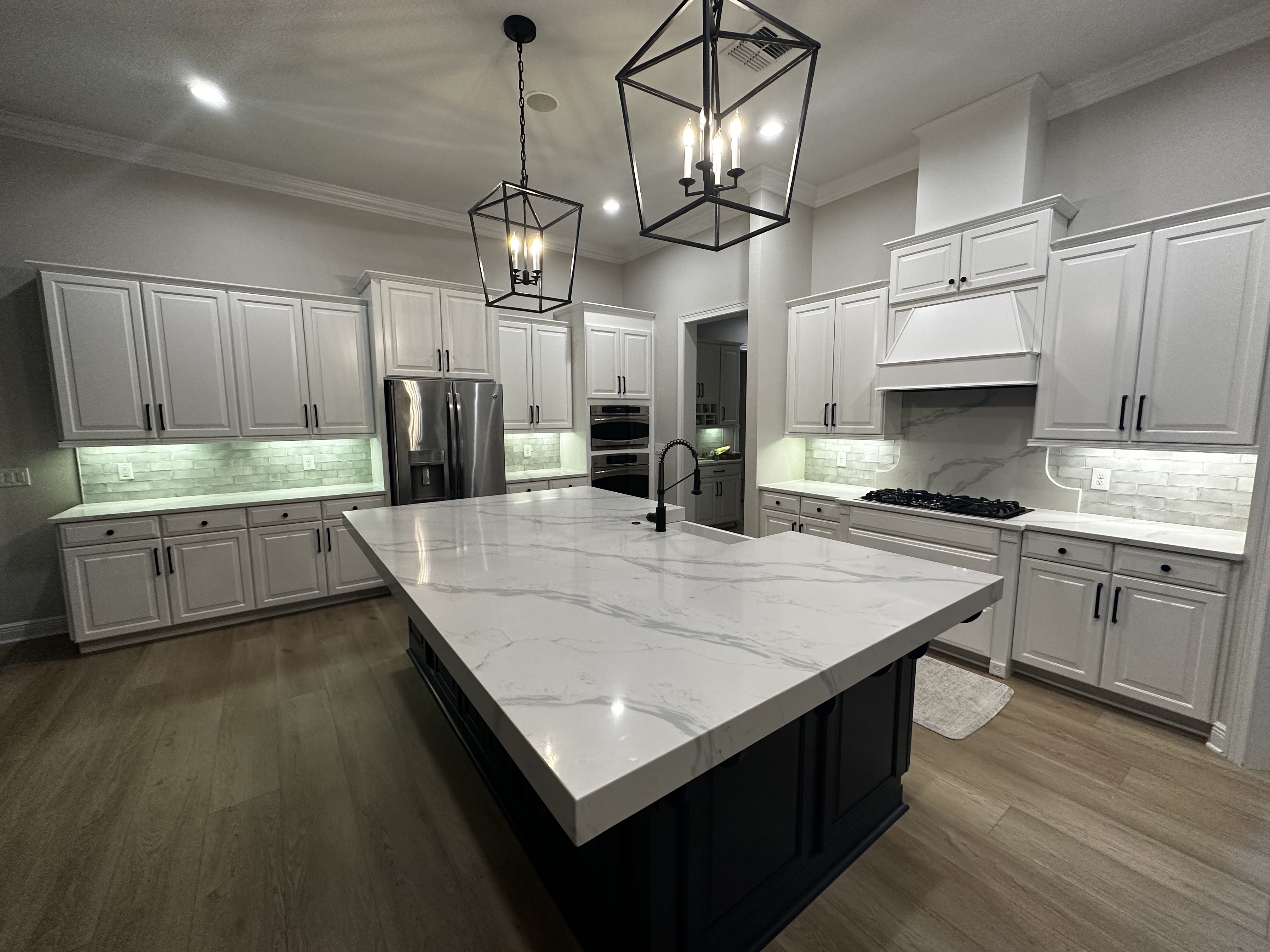 Spacious white kitchen with large marble island, black iron pendant lights, and custom range hood